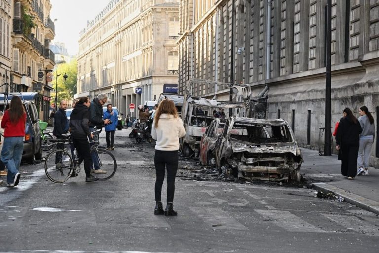 Burned vehicles and debris lining a street in Paris during public protests over economic and public service crises.