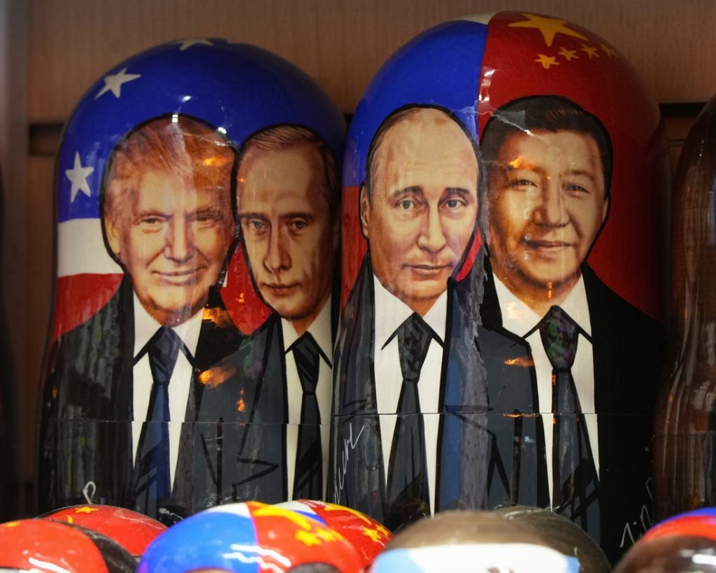 Painted wooden Russian nesting dolls featuring portraits of Donald Trump, Vladimir Putin, and Xi Jinping alongside their national flag designs.