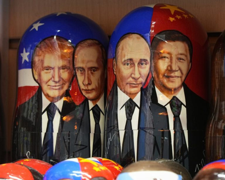 Painted wooden Russian nesting dolls featuring portraits of Donald Trump, Vladimir Putin, and Xi Jinping alongside their national flag designs.
