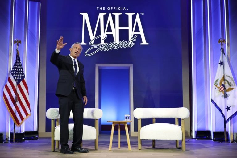 Robert F. Kennedy Jr. waving to an audience on stage in front of a Make America Healthy Again banner.