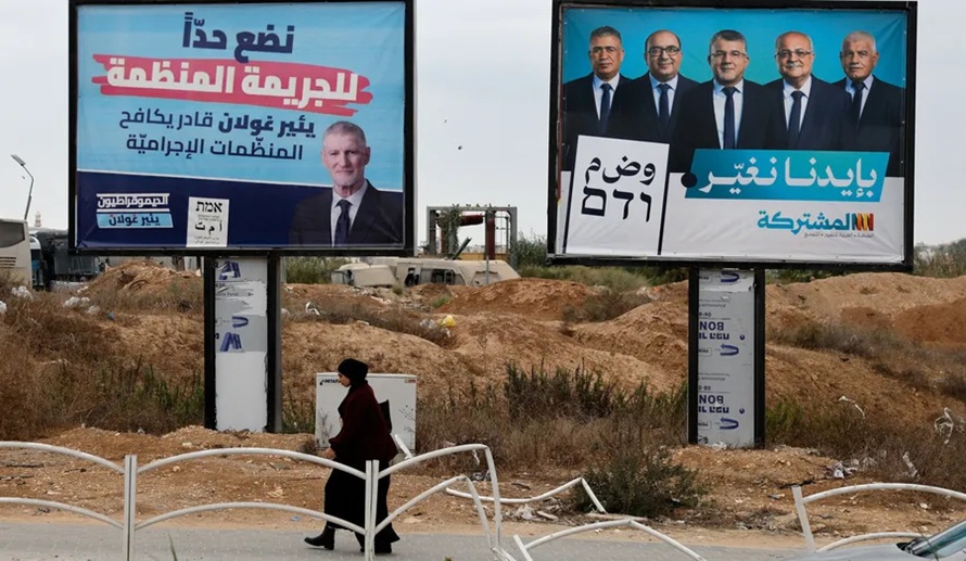 Political billboards in Israel with political figures and text in Hebrew and Arabic, while a woman walks past in the foreground.