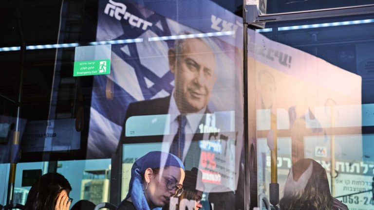 Commuters on a public transit bus with a political campaign poster of Benjamin Netanyahu visible in the window reflection.