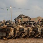 Row of Israeli armored personnel carriers and military vehicles parked in a desert staging area.