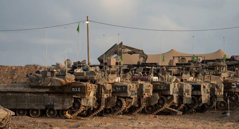 Row of Israeli armored personnel carriers and military vehicles parked in a desert staging area.