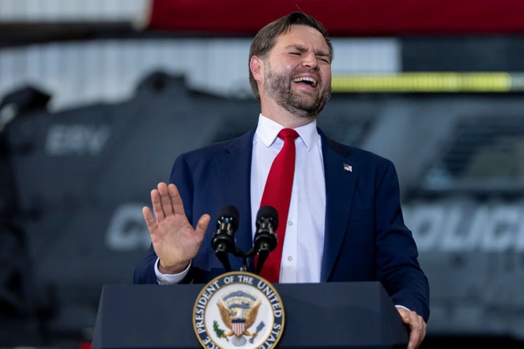 JD Vance speaking behind a presidential podium with a red tie and an expressive gesture.