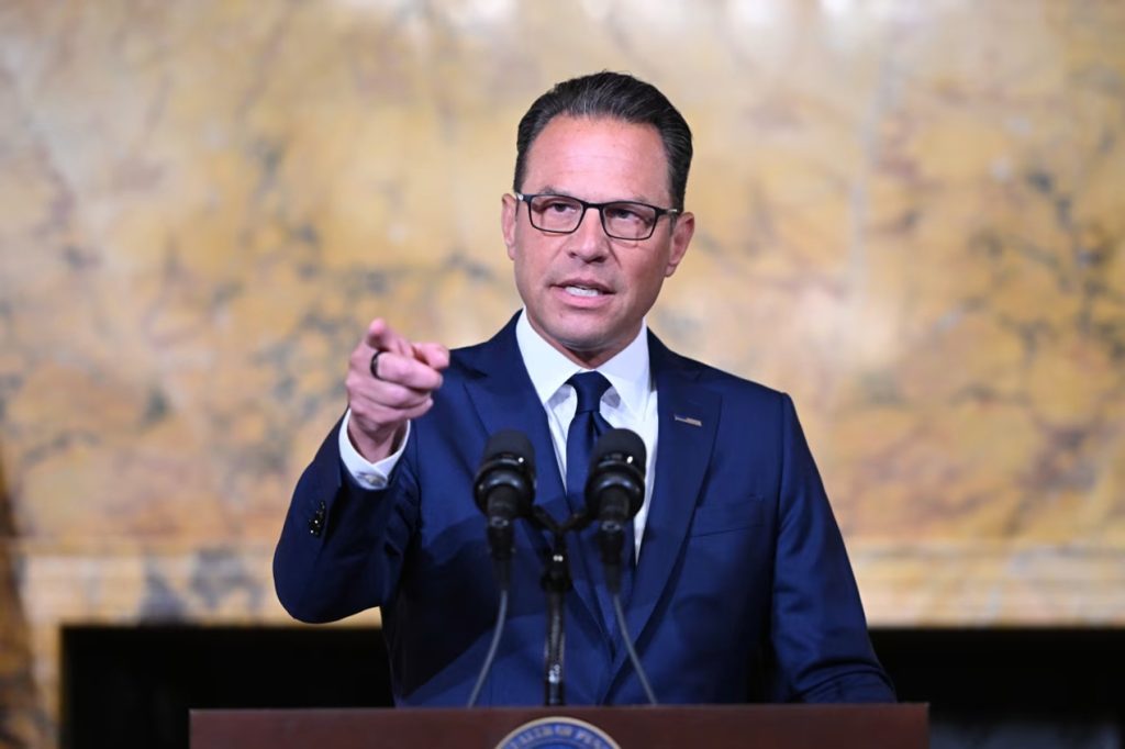 Pennsylvania Governor Josh Shapiro speaking at a podium and gesturing forward with his index finger.