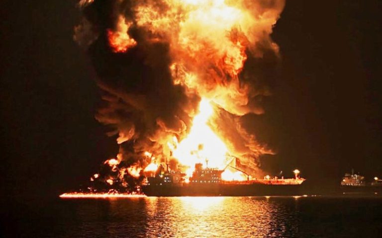Large commercial tanker ship engulfed in flames and massive smoke at night.