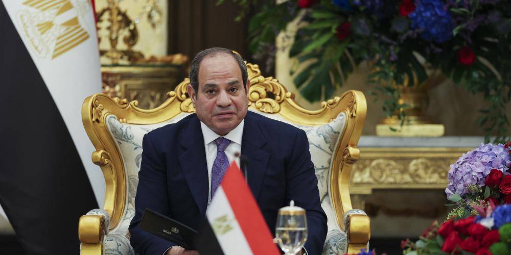 Egyptian President Abdel Fattah el-Sisi seated in an ornate gold armchair with Egyptian flags