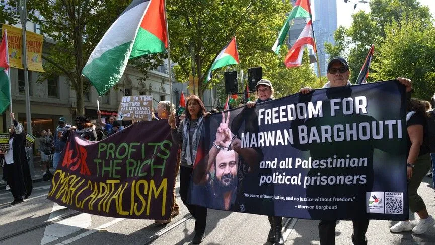 Protesters marching down a city street holding a large banner demanding freedom for Marwan Barghouti and Palestinian political prisoners