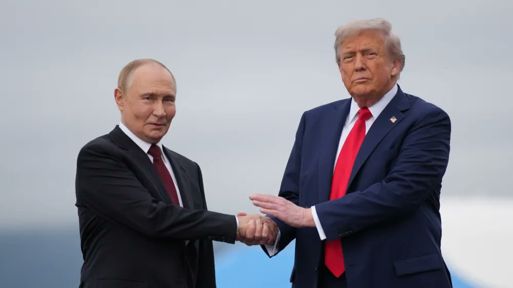 Vladimir Putin and Donald Trump shaking hands outdoors in suits and ties.