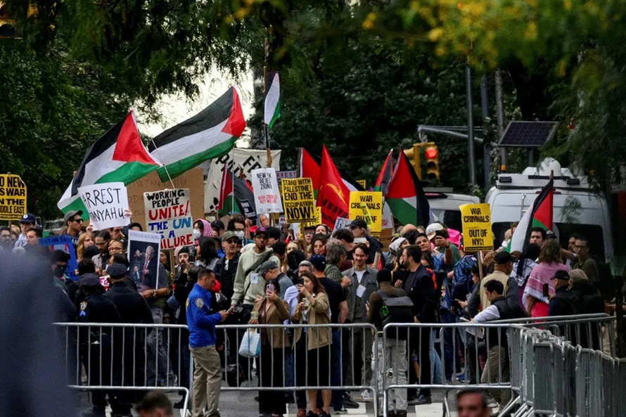 Protesters holding Palestinian flags and demonstration signs behind metal police barricades.