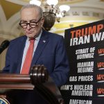 Senator Chuck Schumer speaking at a podium next to a chart criticizing Trump's Iran policy