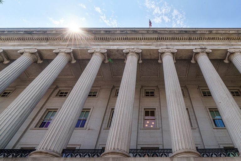 Low-angle view of the classical neoclassical columns of the US Department of the Treasury building under direct sunlight.