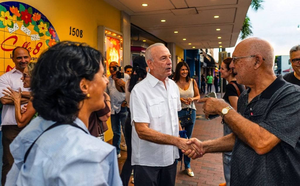 Politicians shaking hands with local residents on a bustling street in Miami.