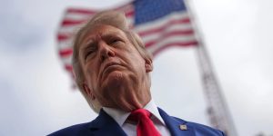 Low-angle portrait of Donald Trump with an American flag waving in the background.