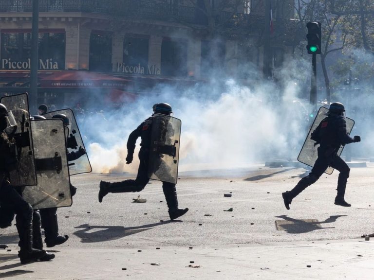 Riot police in tactical gear running through a smoke-filled street during clashes.