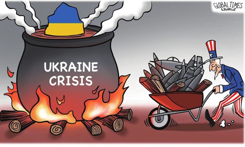 Political cartoon showing Uncle Sam wheeling missiles and artillery into a fire beneath a boiling pot labeled Ukraine Crisis