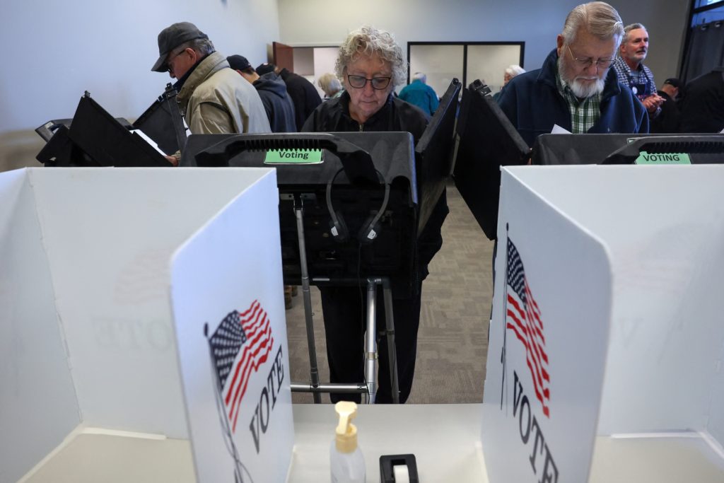 Voters standing at private electronic voting booths with American flag "VOTE" decals on the privacy screens.